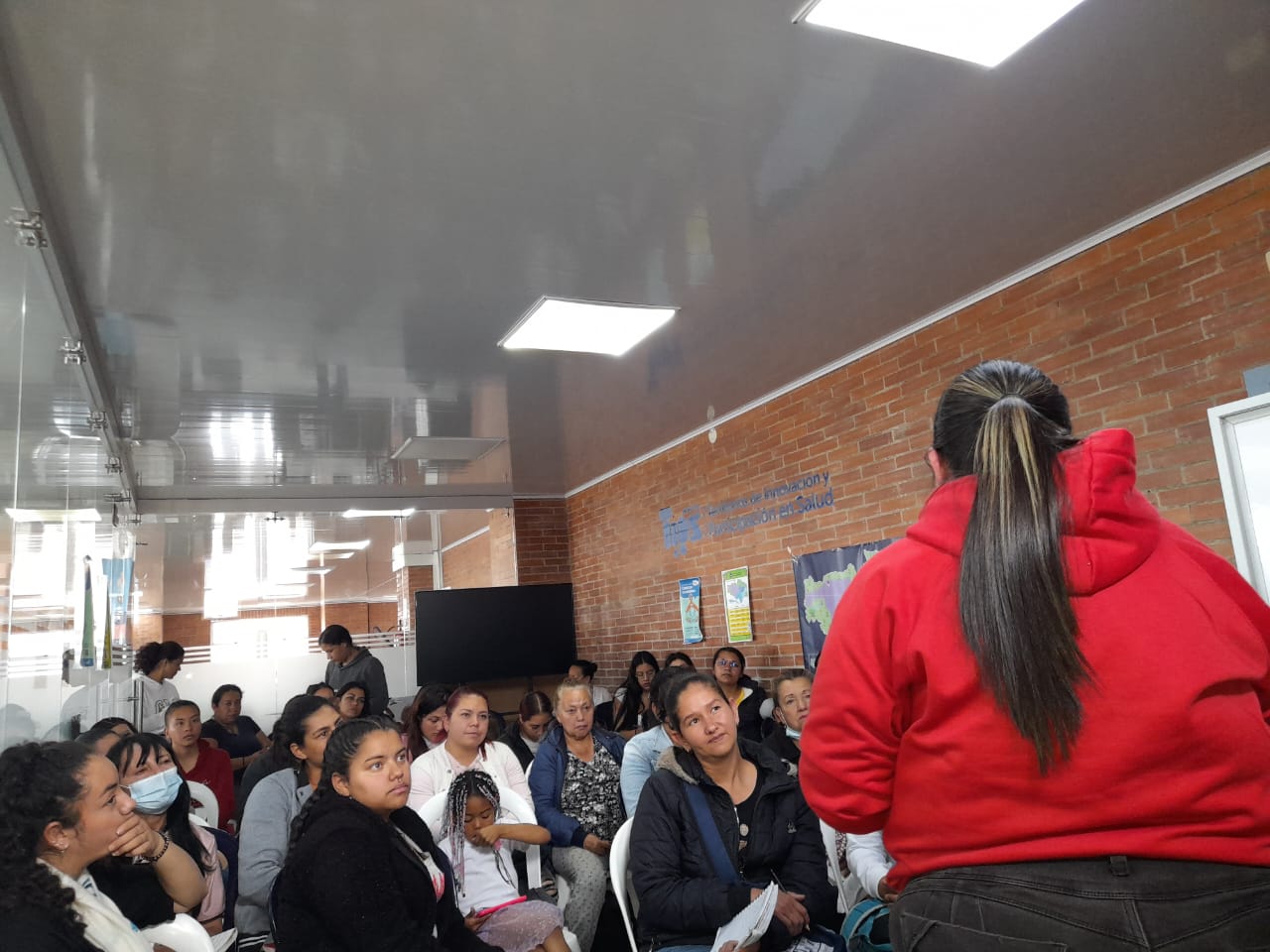 Charla comunitaria con instructora exponiendo frente a asistentes sentadas, Fundación Rosas del Carmelo, Bogotá
