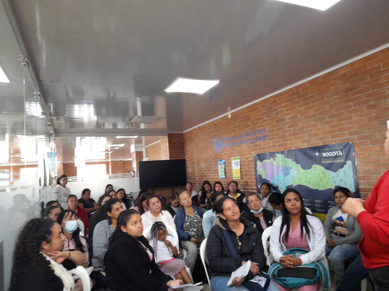 Grupo de mujeres asistiendo a charla comunitaria sentadas en sillas plásticas, Fundación Rosas del Carmelo, Bogotá