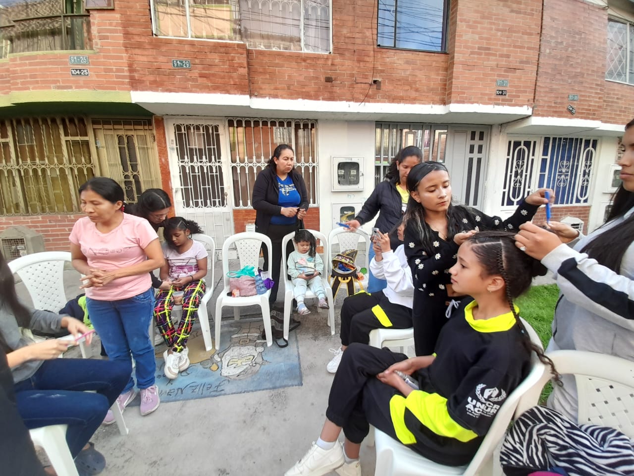 Estudiantes del curso de belleza peinando a niñas en la calle, Fundación Rosas del Carmelo, Bogotá
