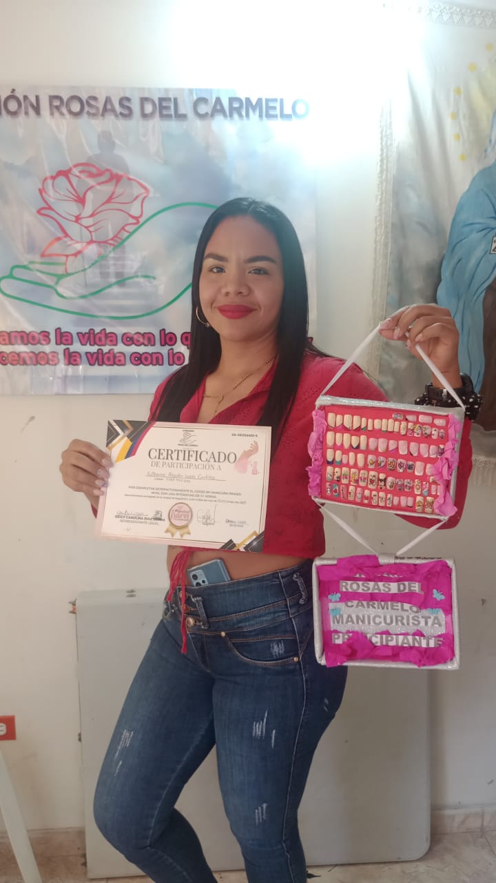Graduada del curso de manicura sosteniendo certificado y exhibidor de uñas decoradas, Fundación Rosas del Carmelo