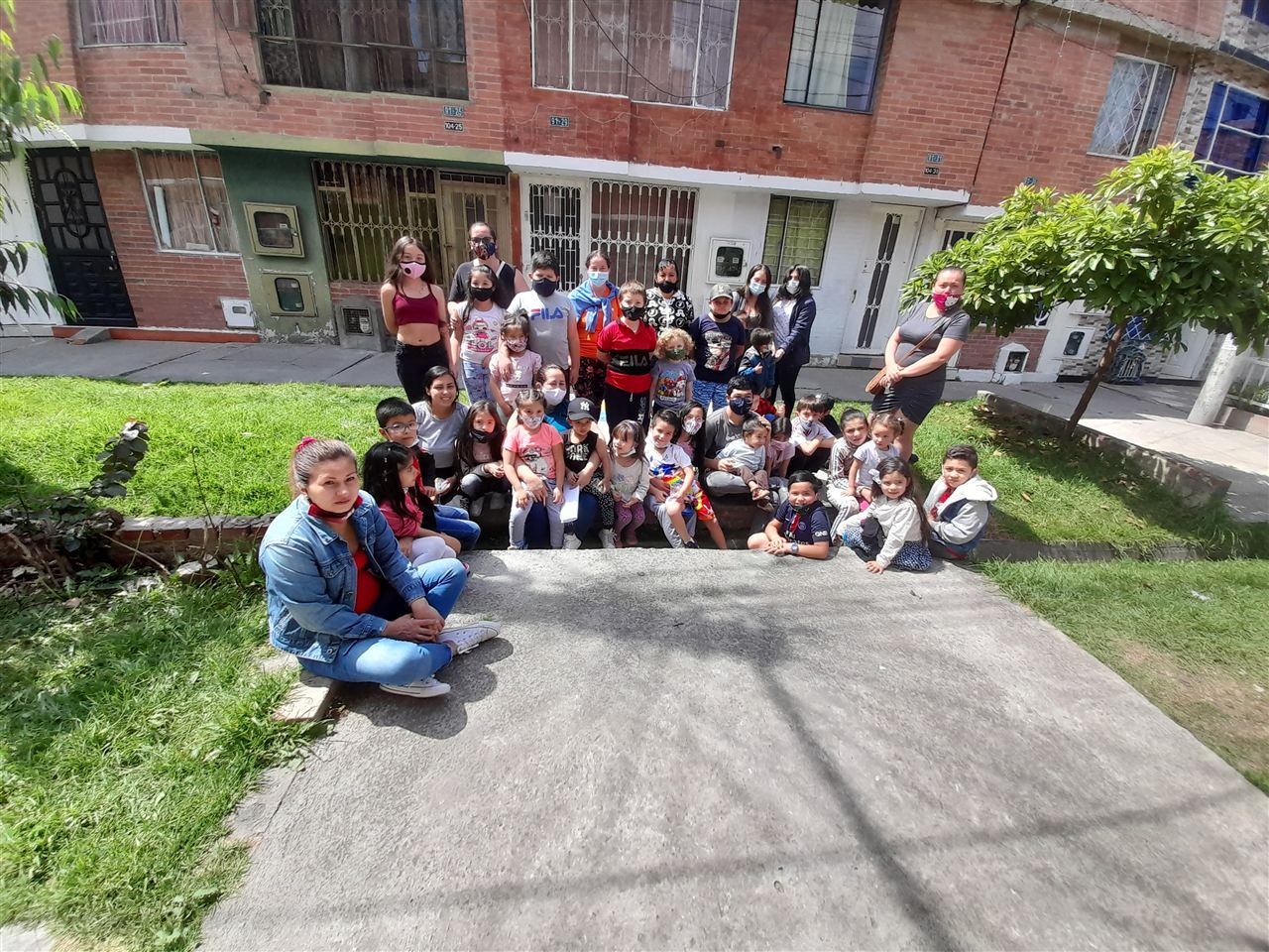 Grupo numeroso de familias reunidas frente a sus viviendas en jornada navideña, Fundación Rosas del Carmelo, Bogotá