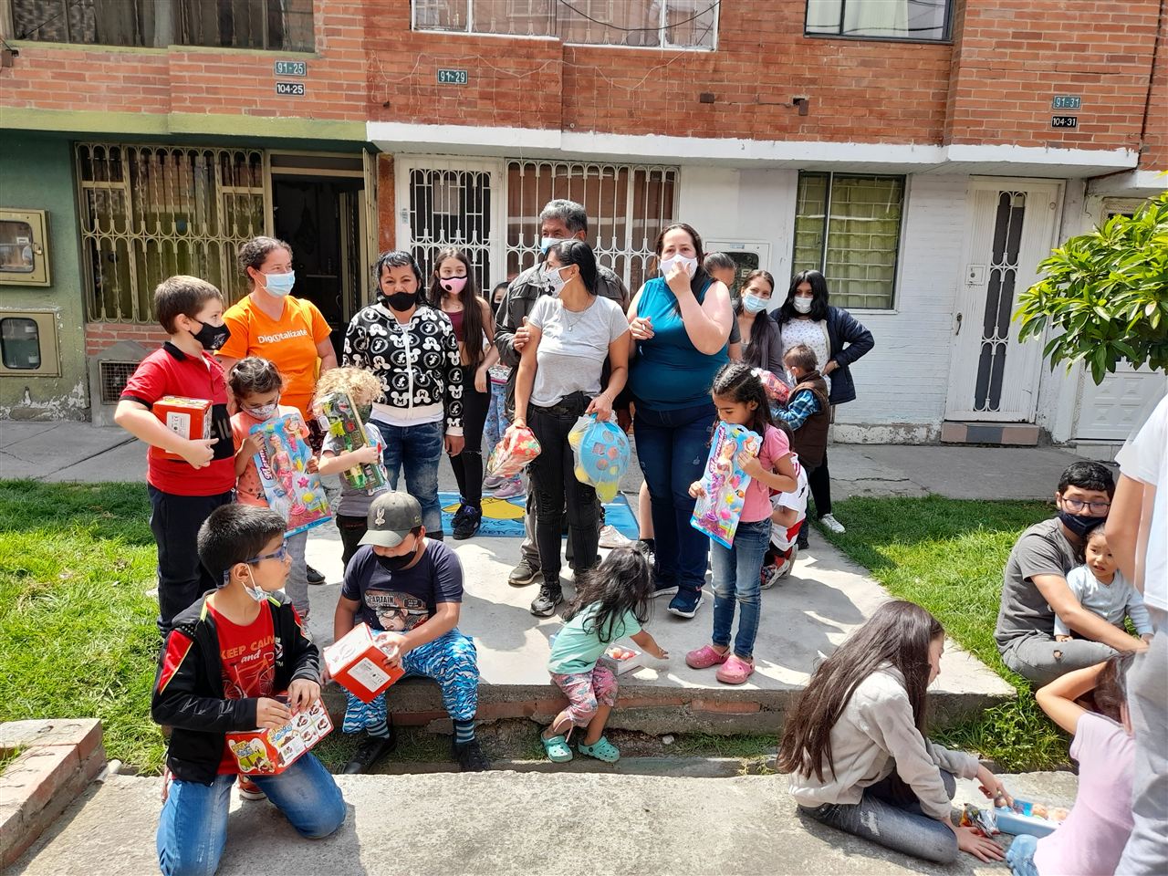 Niños y familias recibiendo regalos frente a sus viviendas en la celebración de Navidad, Fundación Rosas del Carmelo
