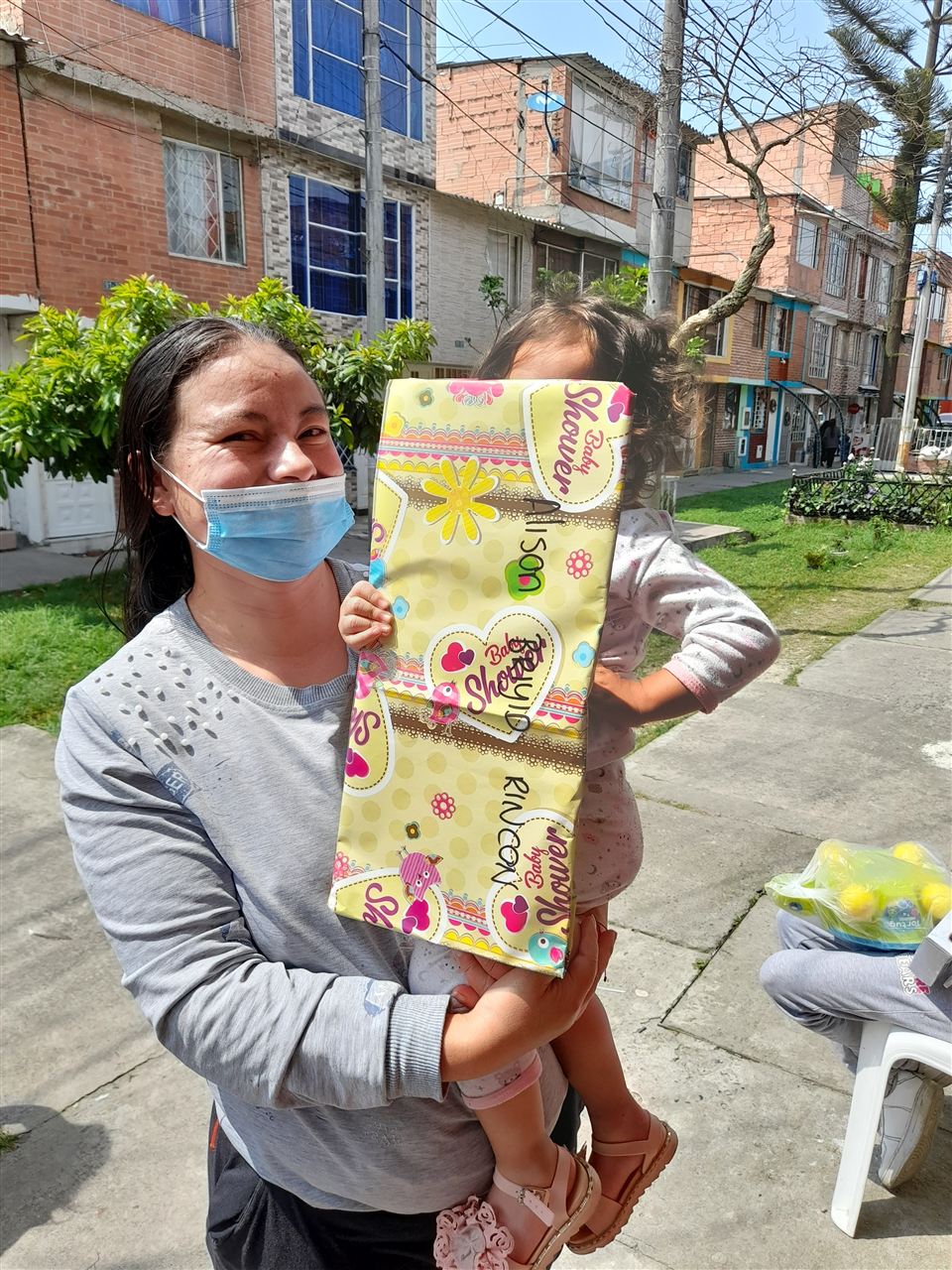 Madre cargando a su hija con un regalo envuelto durante la jornada navideña, Fundación Rosas del Carmelo, Bogotá