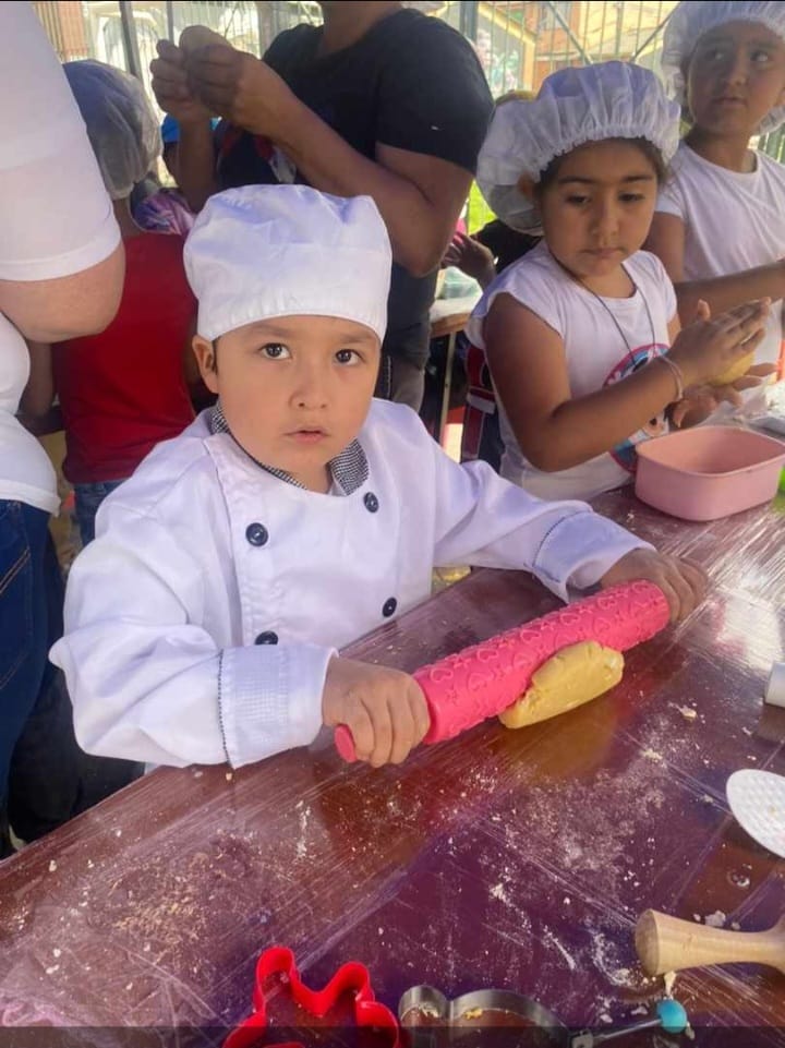 Niño vestido de chef estirando masa con rodillo en el curso de pastelería, Fundación Rosas del Carmelo
