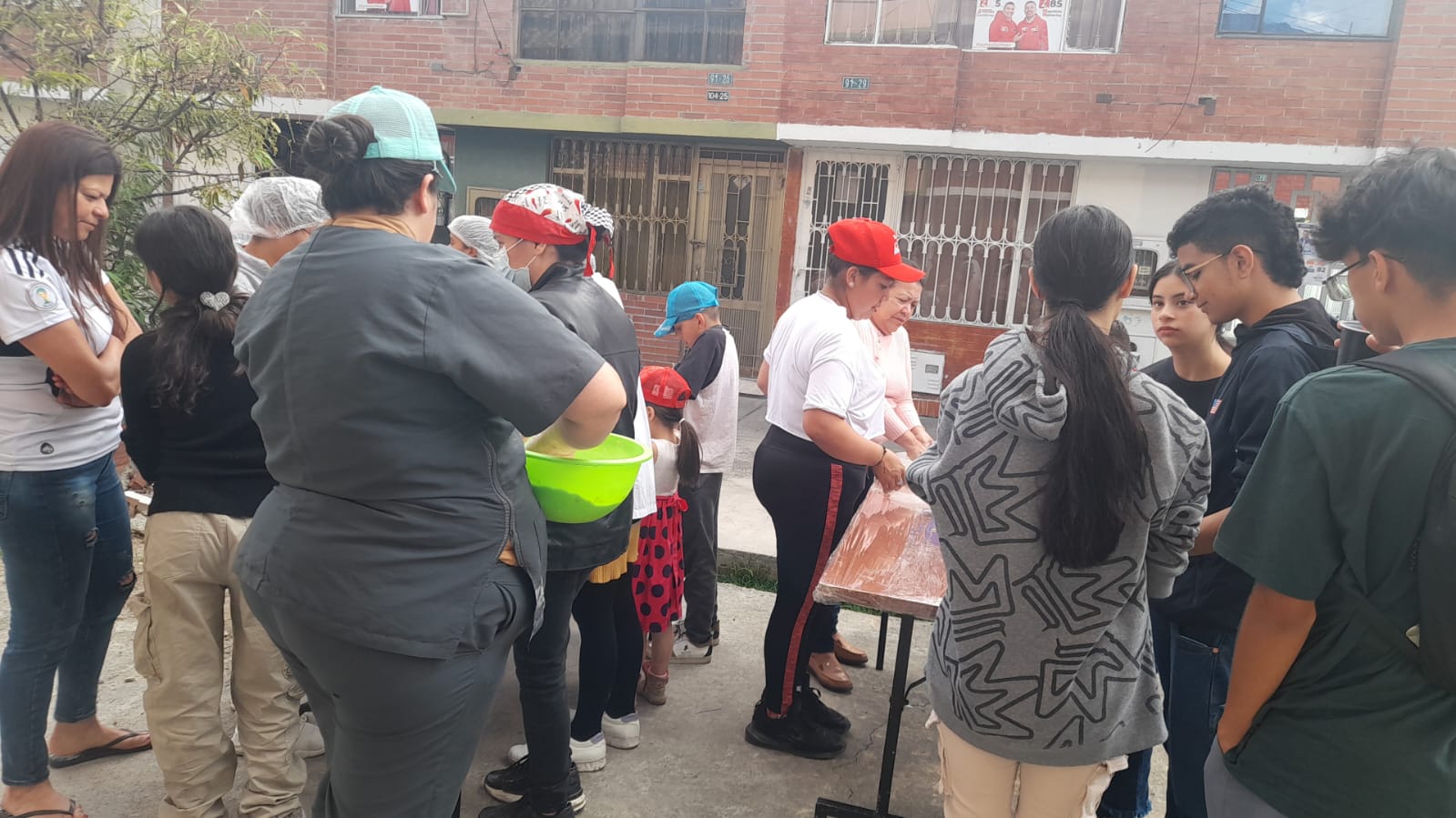 Grupo preparando masa de pastelería en mesa al aire libre frente a casas de un barrio de Bogotá