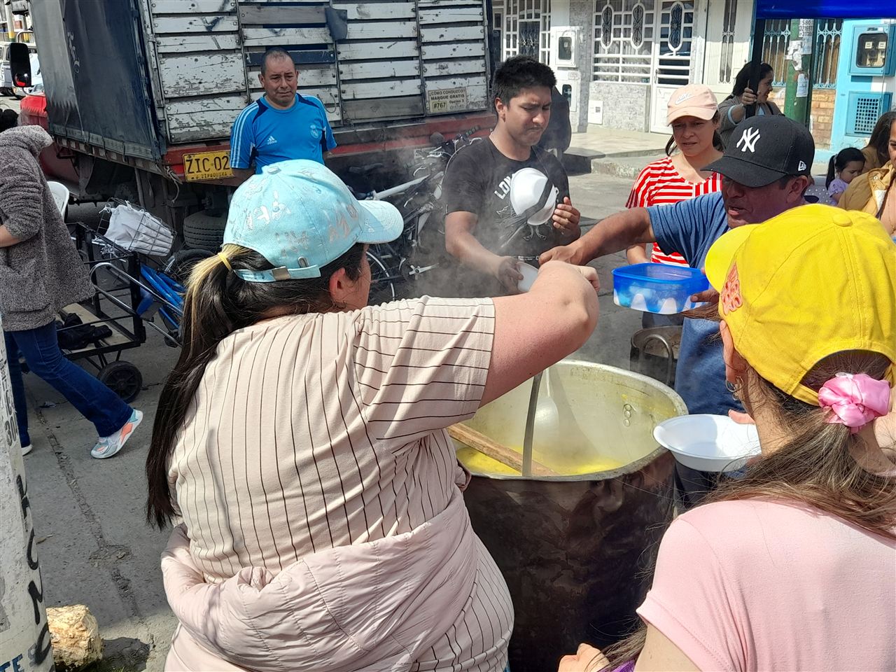 Voluntario sirviendo sancocho con cucharón desde una olla grande junto a un camión, Fundación Rosas del Carmelo, Bogotá