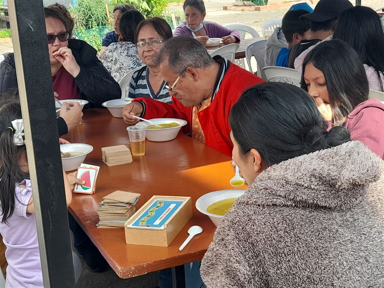 Familia comiendo sancocho y jugando cartas en una mesa comunitaria, Fundación Rosas del Carmelo, Bogotá
