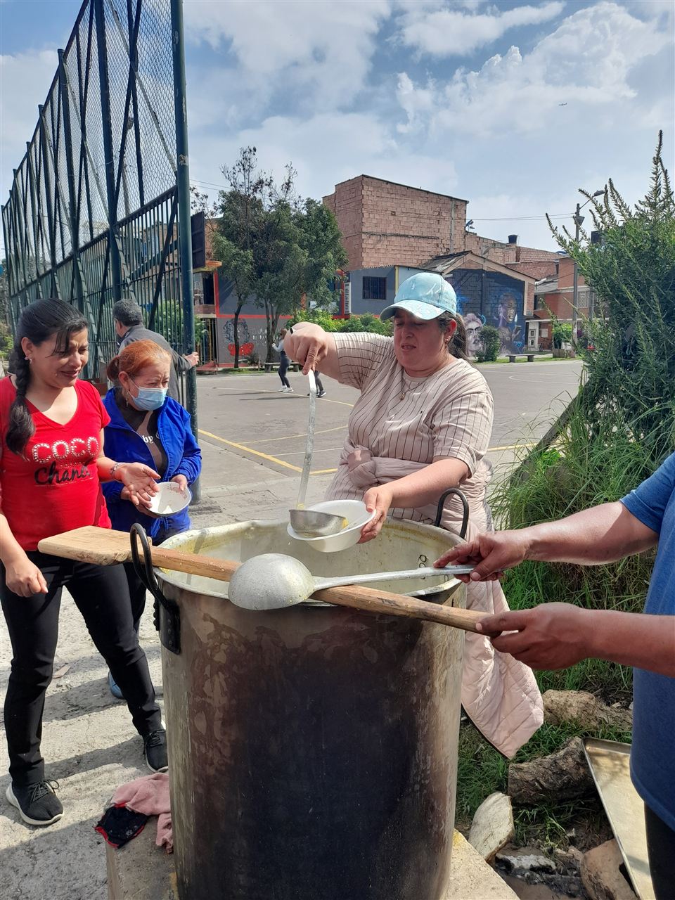 Voluntaria sirviendo sancocho a una asistente con tapabocas junto a una olla grande, Fundación Rosas del Carmelo, Bogotá