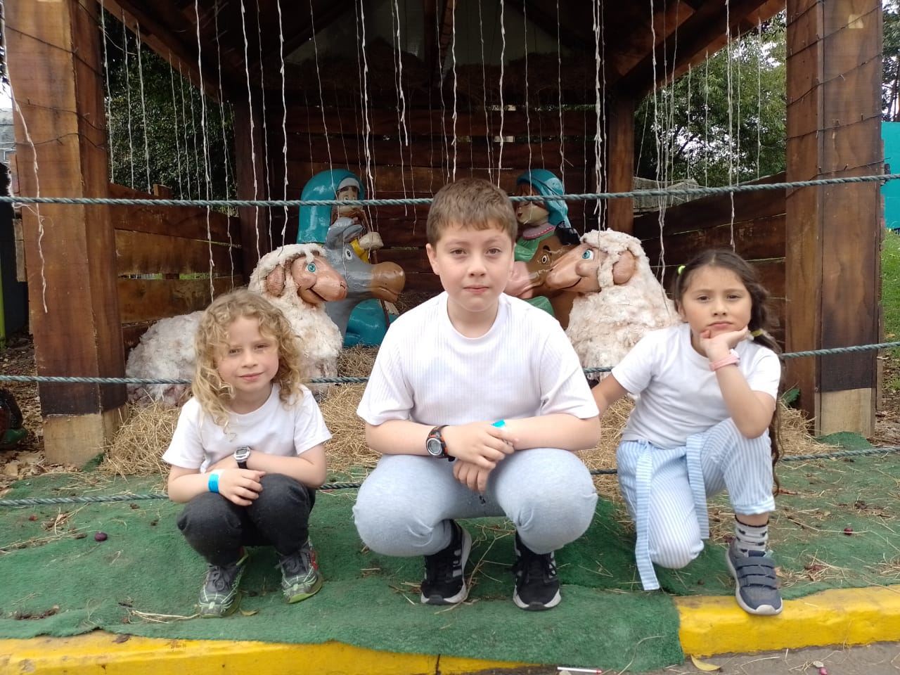 Niños posando junto a un pesebre navideño de madera durante las Vacaciones Recreativas, Fundación Rosas del Carmelo, Bogotá