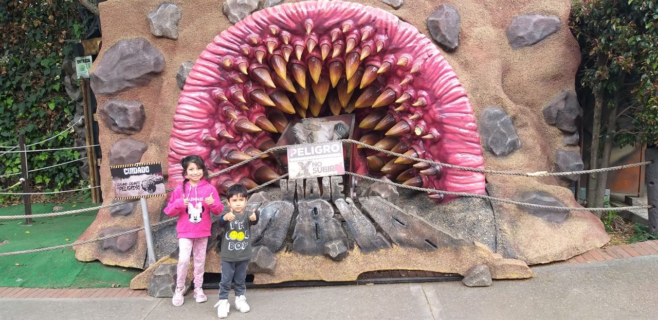 Niños posando frente a la entrada temática de dinosaurio del parque durante las Vacaciones Recreativas, Fundación Rosas del Carmelo